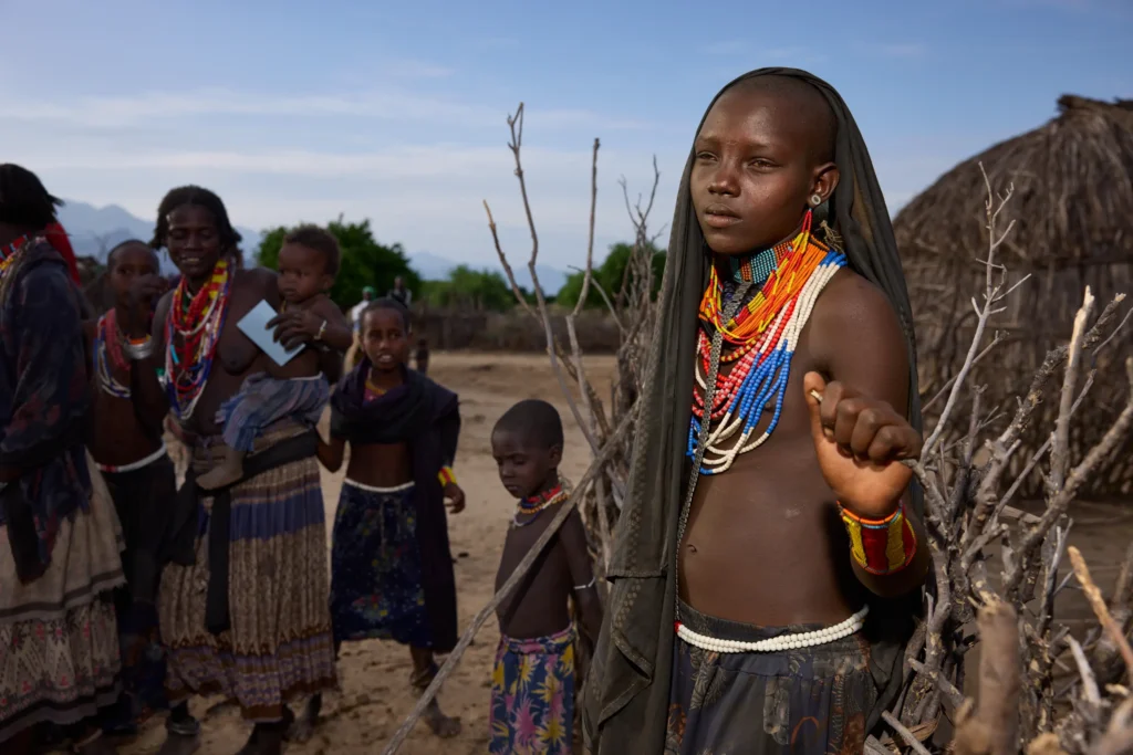Arbore girl wearing traditional beadwork and metal bracelets standing near tree in Ethiopia | Michaela Pupíková Photography
