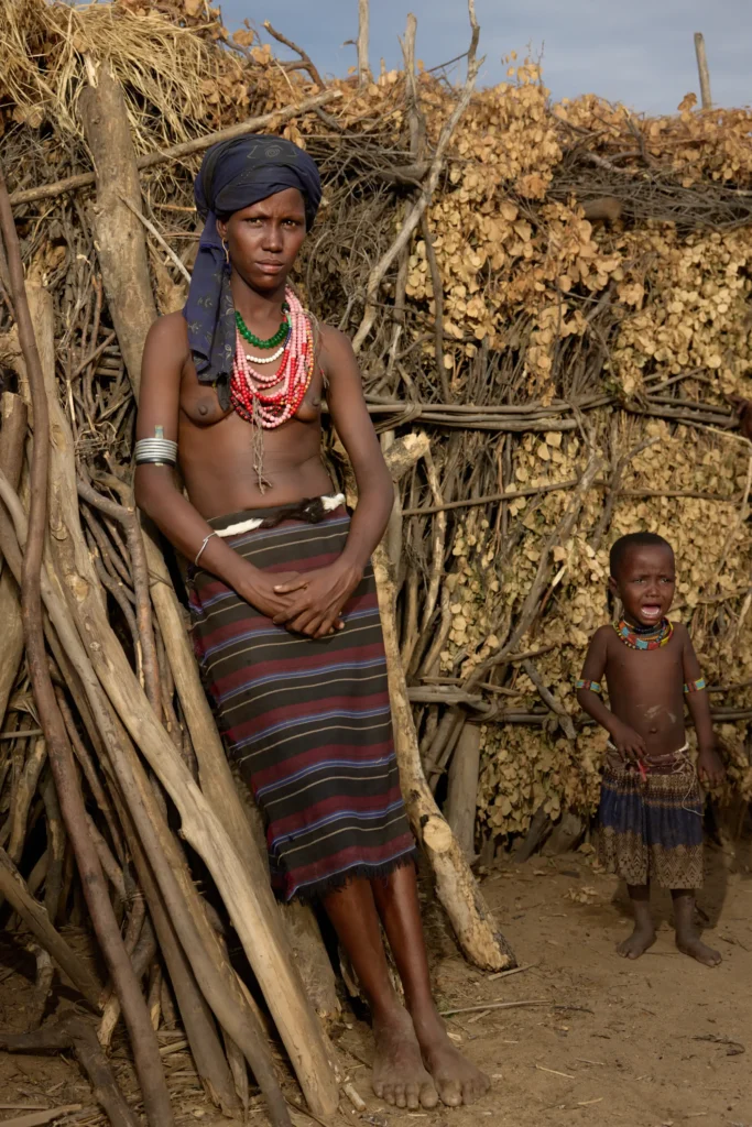Young Arbore woman and child posing in front of firewood stack in village, Ethiopia | Michaela Pupíková Photography