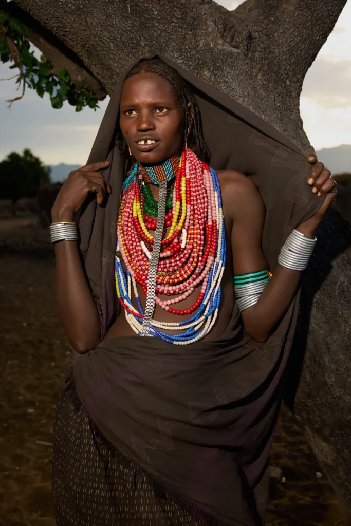 Arbore woman wearing traditional beadwork and metal bracelets standing near tree in Ethiopia | Michaela Pupíková Photography