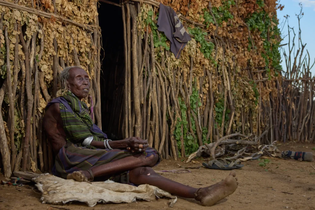 Elder Dassanech woman resting in front of wooden fence structure in Dassanech village, Ethiopia | Michaela Pupíková Photography