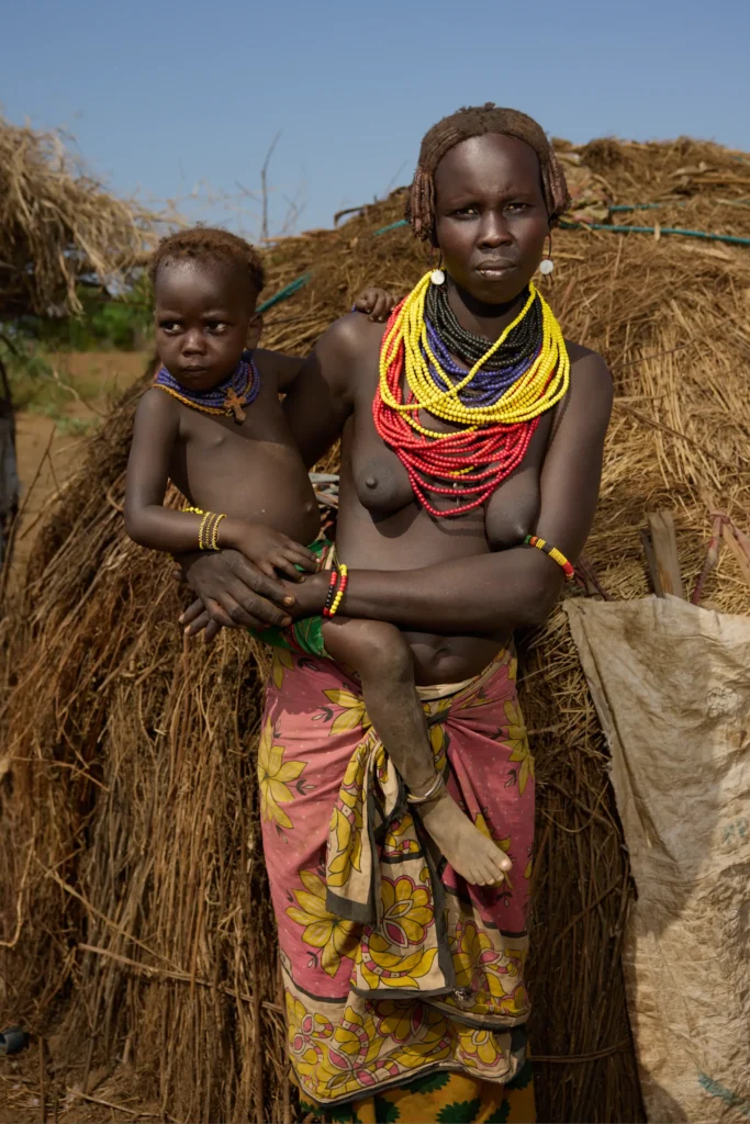 Dassanech woman carrying child in front of straw hut in southern Ethiopia | Michaela Pupíková Photography