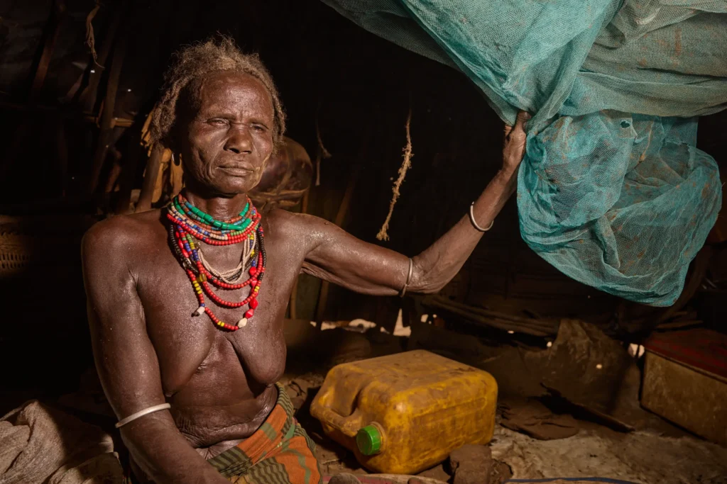 Elder Dassanech woman holding mosquito net inside hut in tribal Ethiopia | Michaela Pupíková Photography