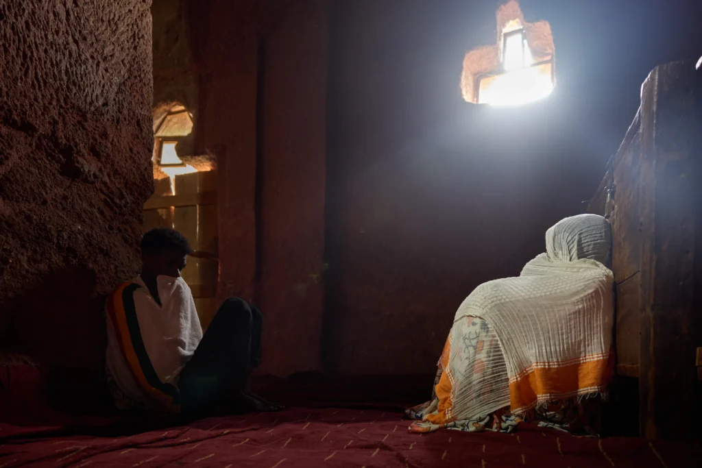 Ethiopian monk meditating near sunlit doorway in Lalibela rock-hewn church | Michaela Pupíková Photography