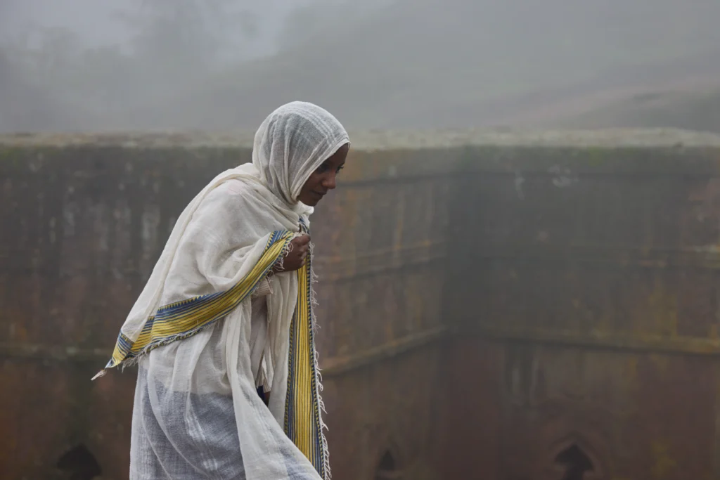 Monk walking through rock-hewn corridor of a Lalibela church lit by sunlight | Michaela Pupíková Photography