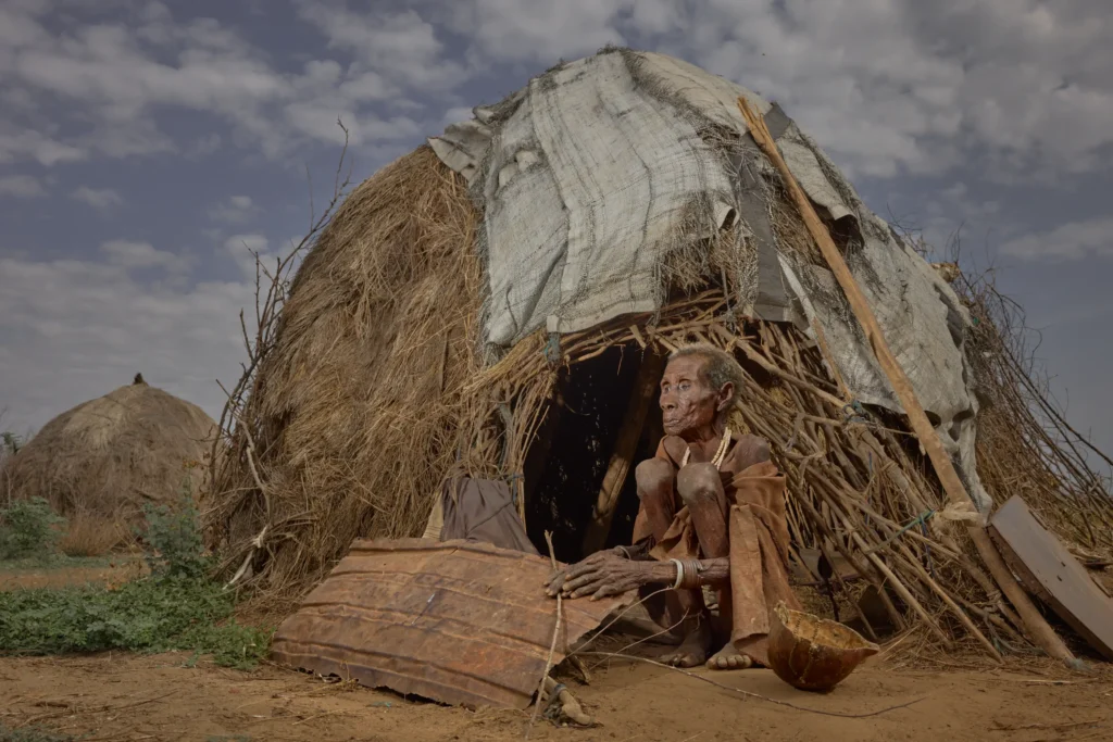Nyangatom woman sitting outside tarp-covered shelter in rural Nyangatom village, Ethiopia | Michaela Pupíková Photography