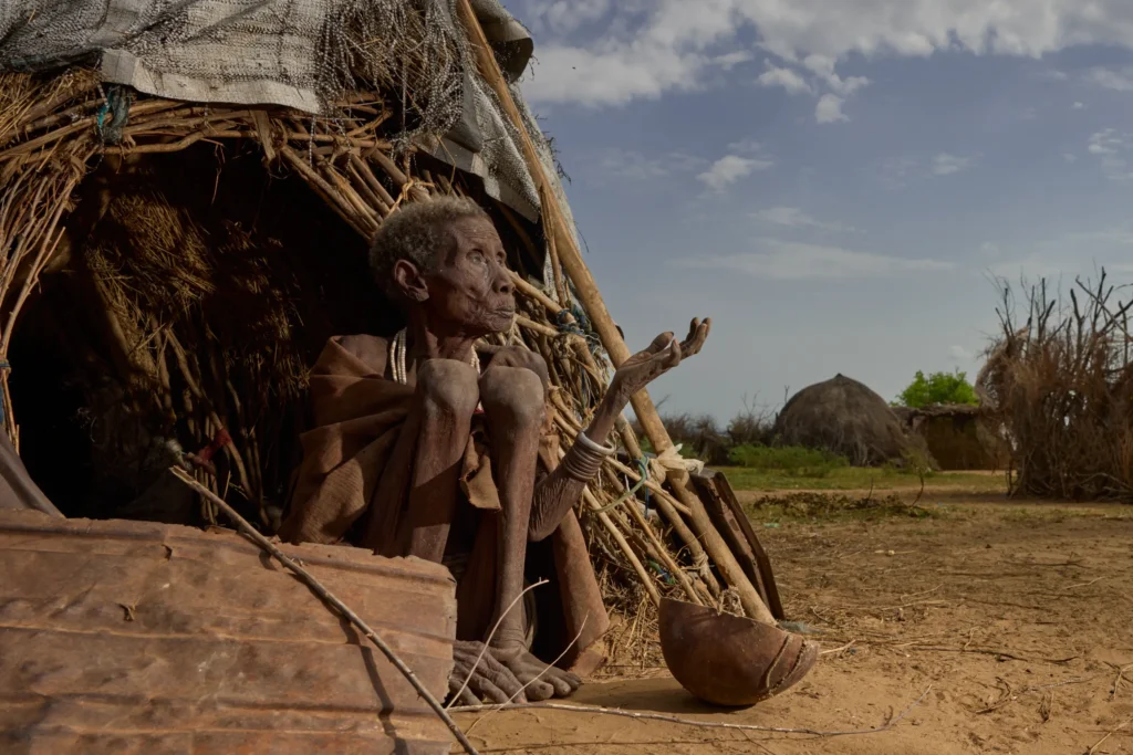 Nyangatom woman sitting at hut entrance with cooking tools in rural village, Ethiopia | Michaela Pupíková Photography