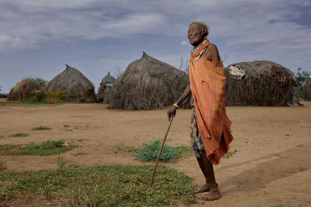 Elder Nyangatom woman walking with stick through dry landscape in tribal Ethiopian village | Michaela Pupíková Photography
