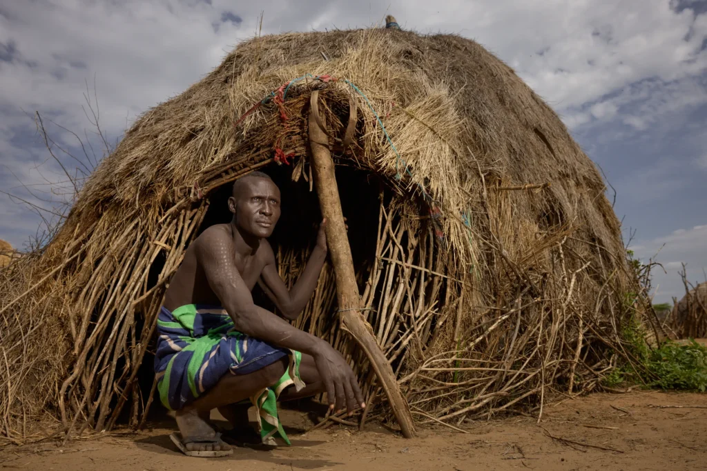 Decorated Nyangatom elder sitting at wooden fence gate in Ethiopian tribal village | Michaela Pupíková Photography