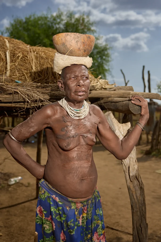 Nyangatom woman with scarification carrying clay bowl on her head in Nyangatom village, Ethiopia | Michaela Pupíková Photography