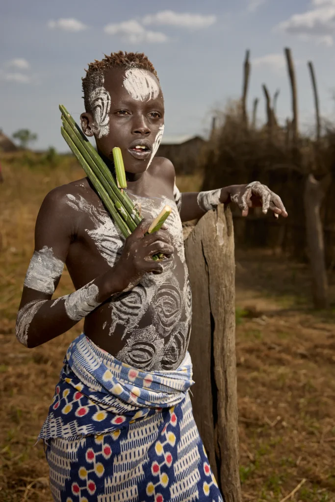 Young Nyangatom boy with ceremonial body paint holding green stalks in rural Ethiopia | Michaela Pupíková Photography