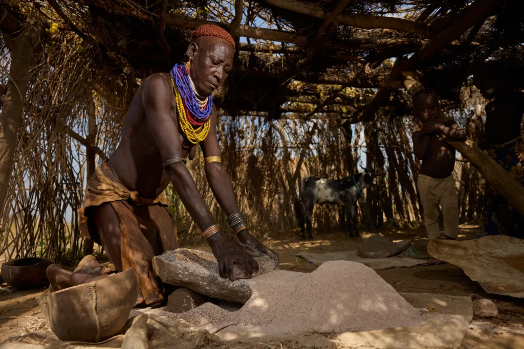 Nyangatom woman working on leather on wooden fence in Ethiopian tribal village | Michaela Pupíková Photography
