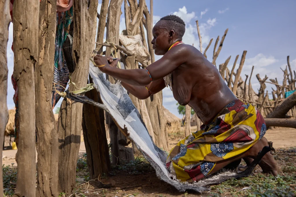 Nyangatom woman working on leather on wooden fence in Ethiopian tribal village | Michaela Pupíková Photography